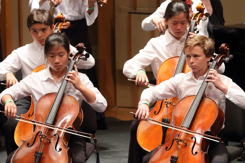 Young students in rows on stage performing cello