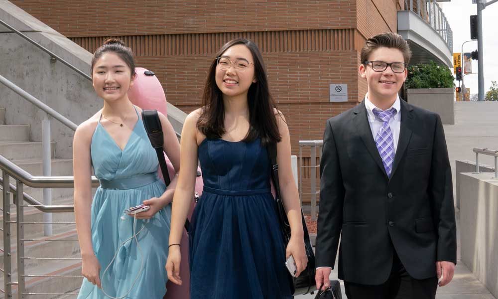 Three high school age students walking down steps. One is in a suit and two are in dresses.