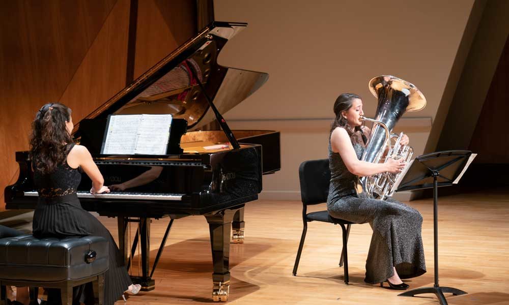 A tuba player in a dress performing with a piano accompanist.