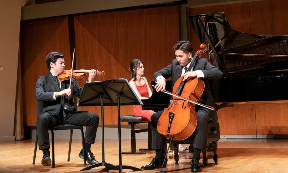 A cellist and a violinist playing in front of a piano accompanist.