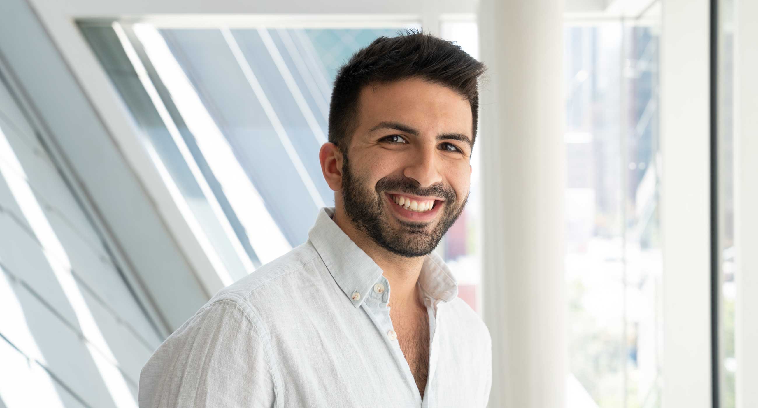 Can Canbolat wearing a collared shirt and smiling in front of a window.