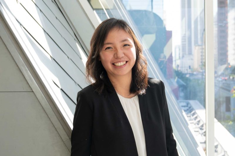 Hui Wu smiling in front of a window, wearing a blazer and a blouse.