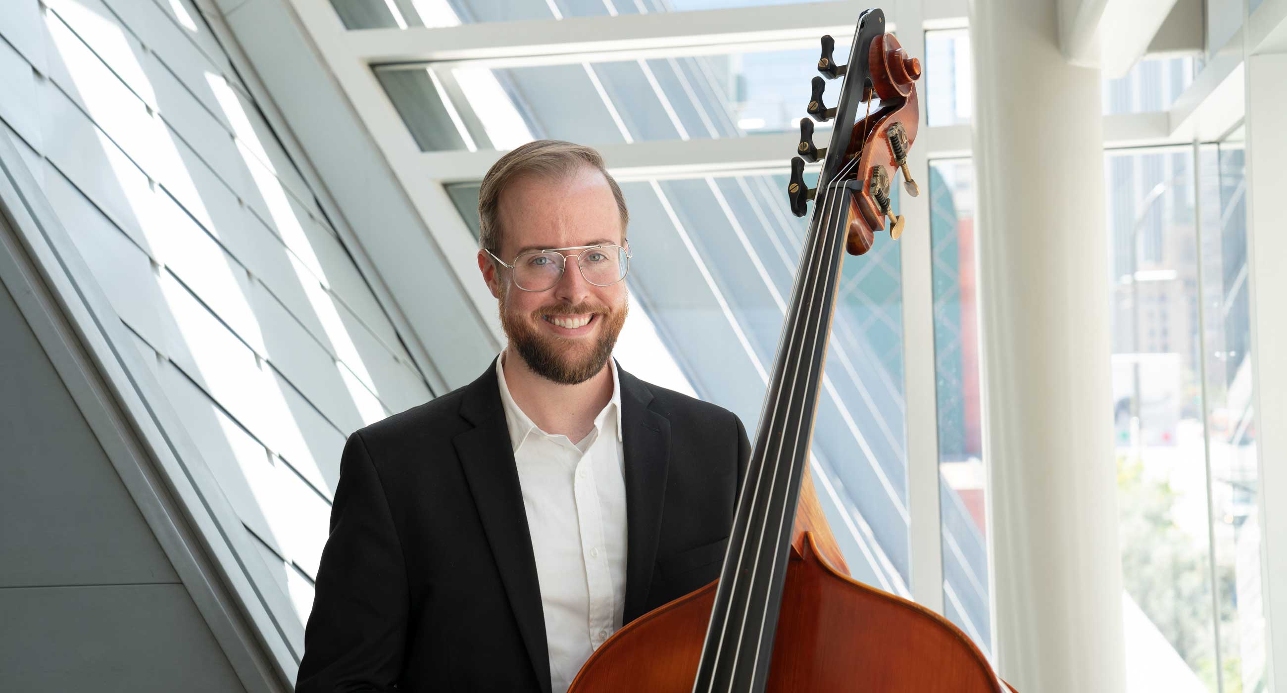 Ryan Emerson Baird holding a bass and smiling in front of a window.