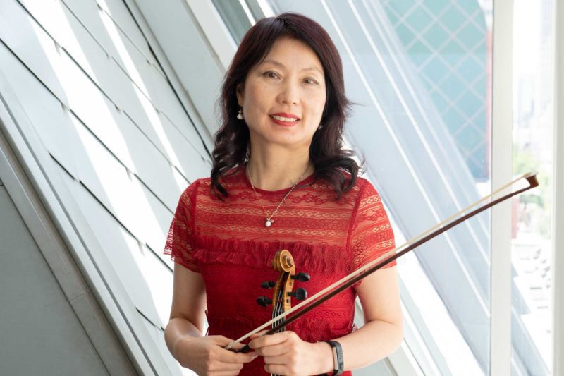 Shih Lan Liu holding a violin and smiling in front of a window.