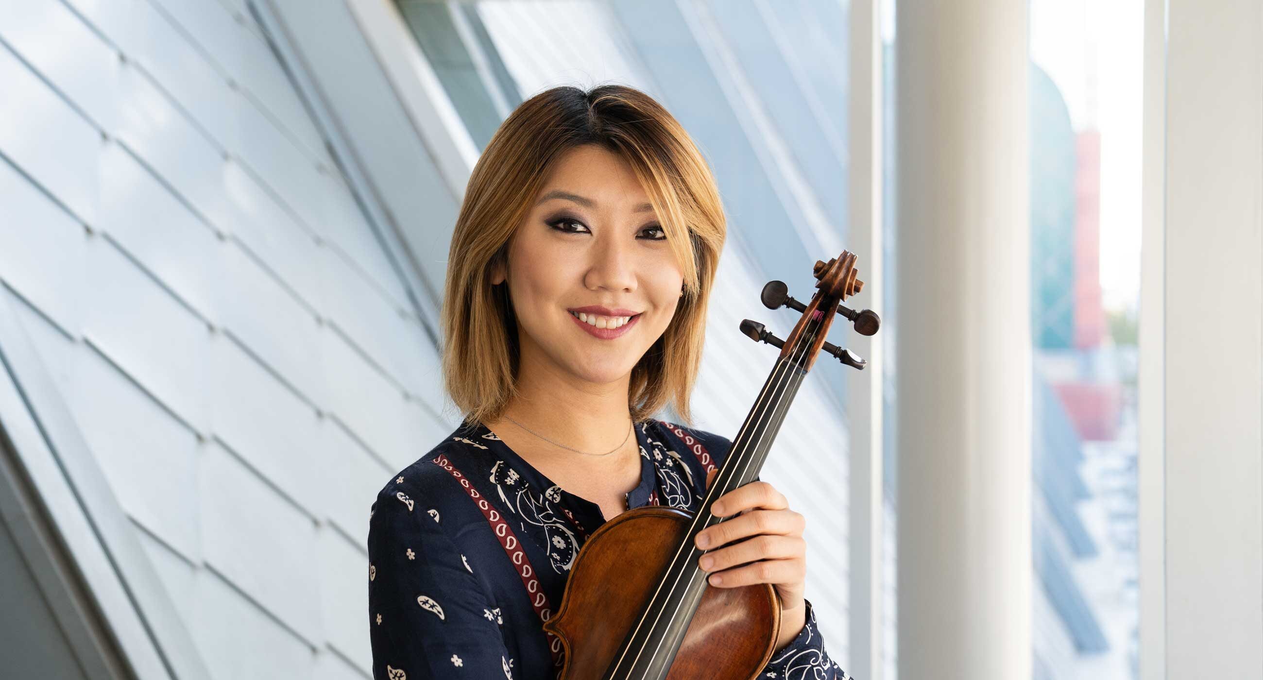 Headshot of Fabiola Kim holding a violin in front of window