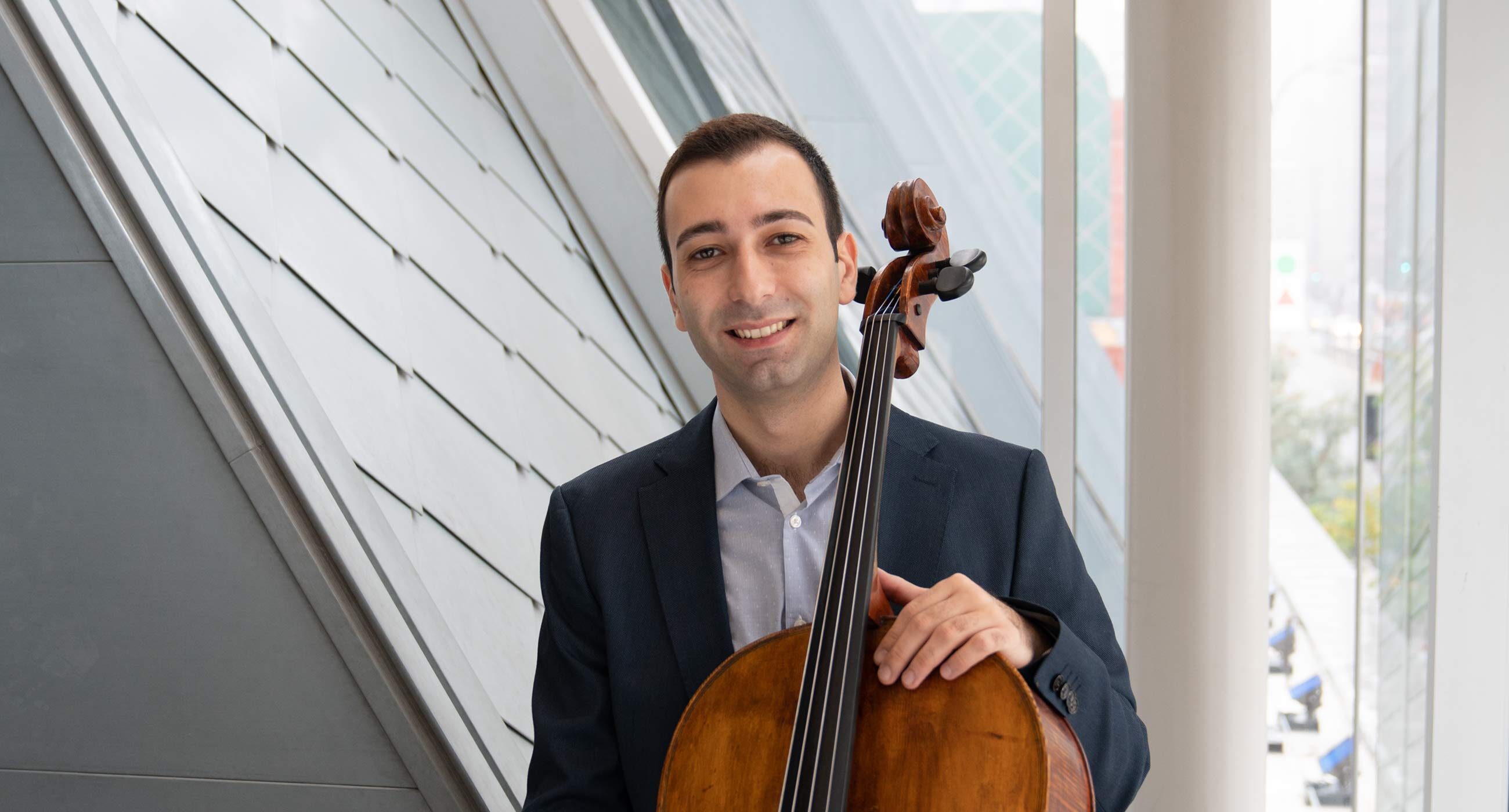 Headshot of Vardan Gasparyan standing in front of a window with a cello