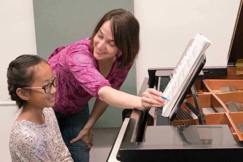 Teacher standing next to a student at a piano