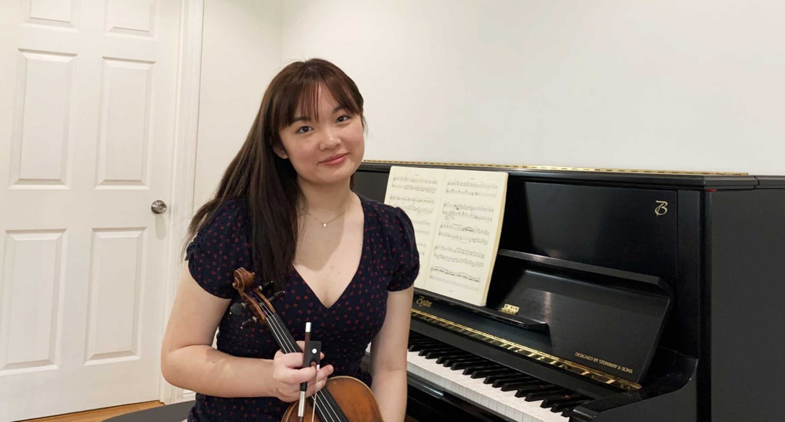 Scarlett Chen holding a violin sitting at a piano