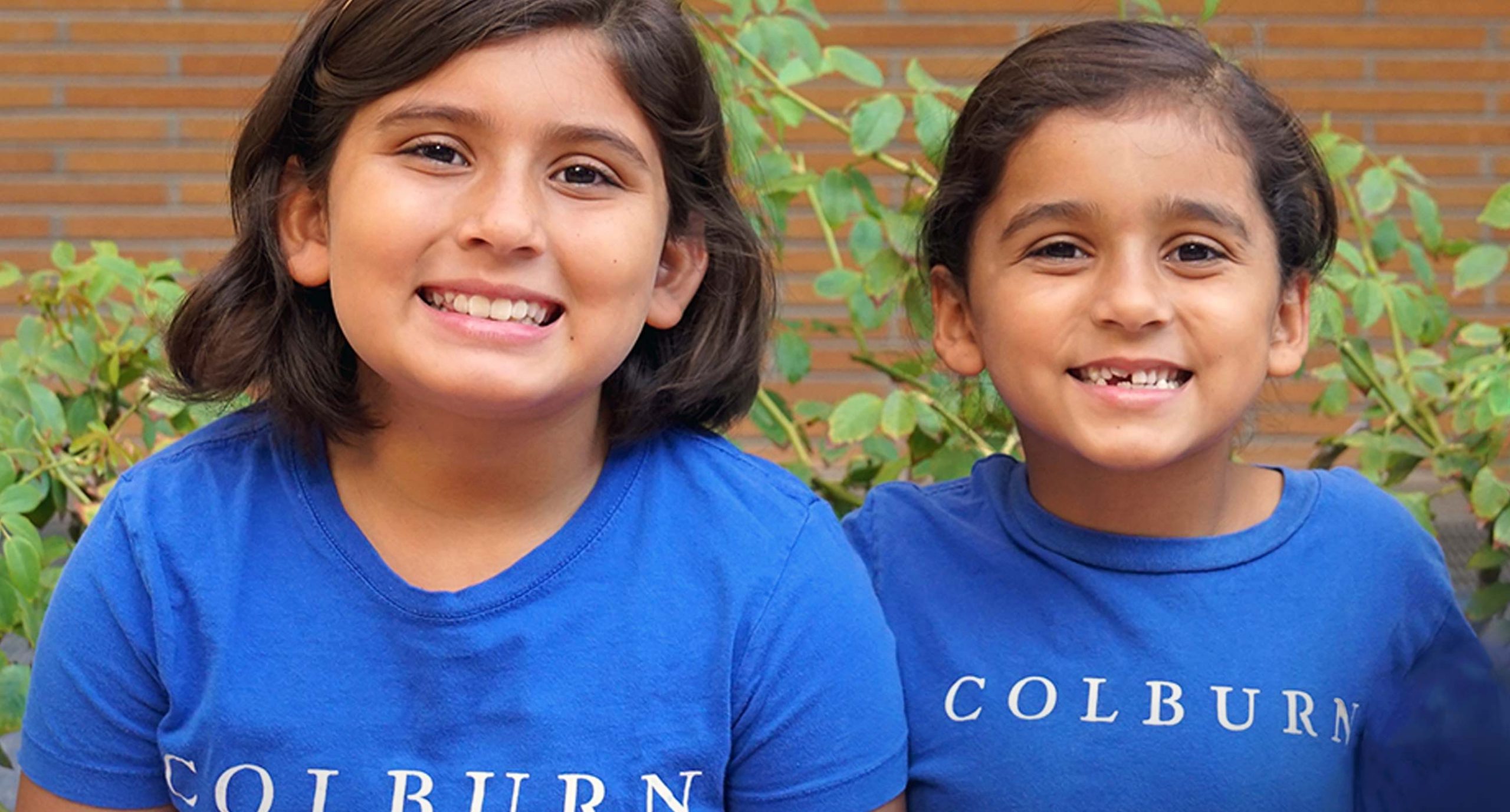 Two young students wearing blue Colburn tshirts smiling