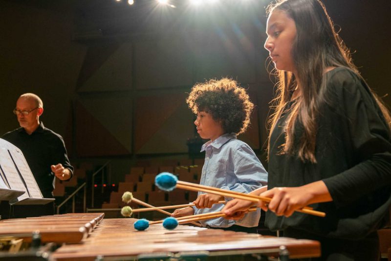 Two students playing marimba on stage with teacher in background