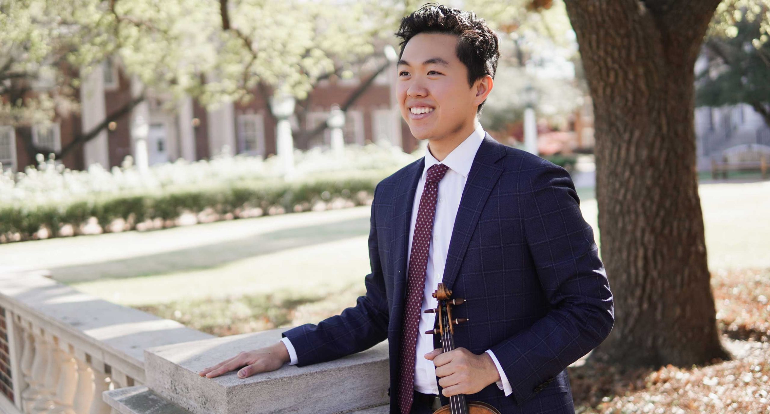 Hao Zhou wearing a suit holding a violin smiling
