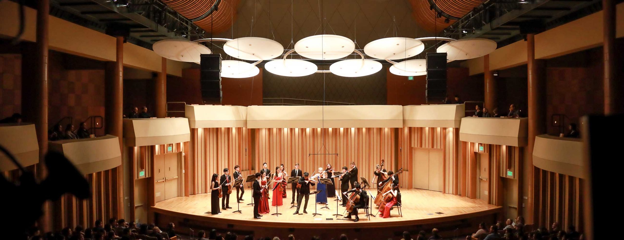 Chamber orchestra in formal dress standing on Zipper Hall stage with full audience