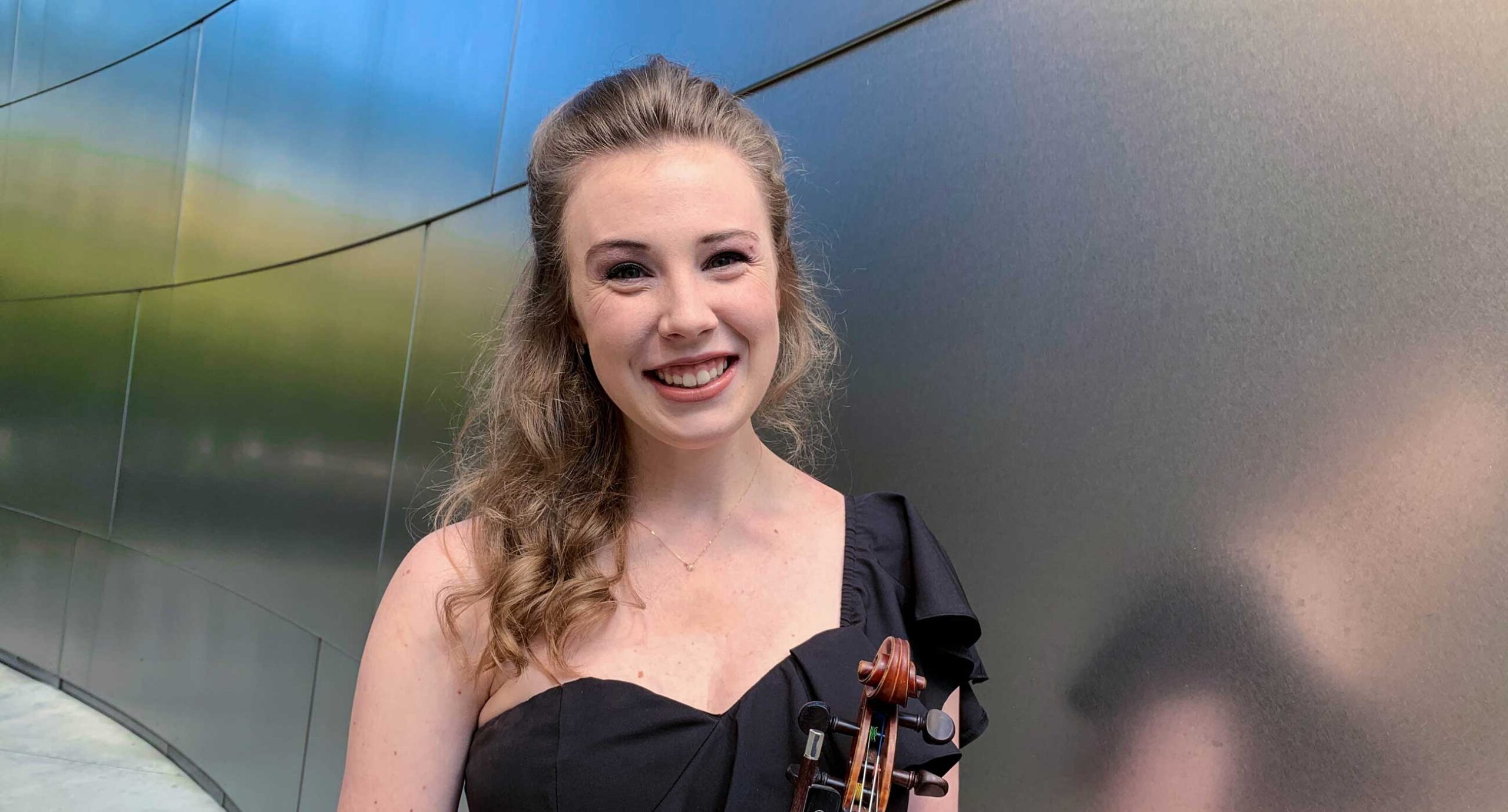 Fiona Shea wearing a black dress holding a violin in front of Walt Disney Concert Hall walls